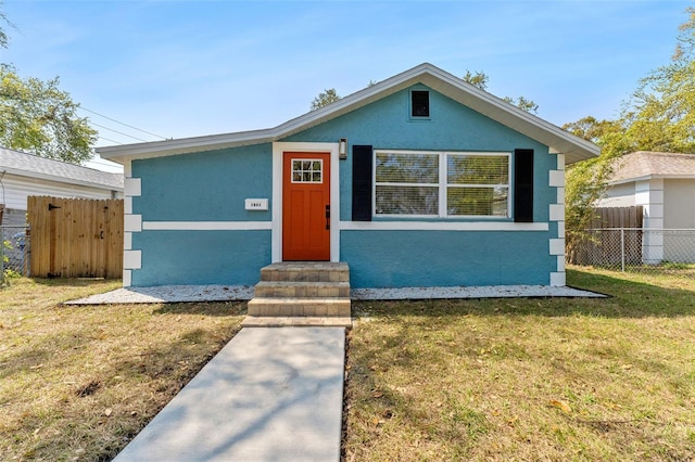 bungalow-style home featuring a front lawn, fence, and stucco siding