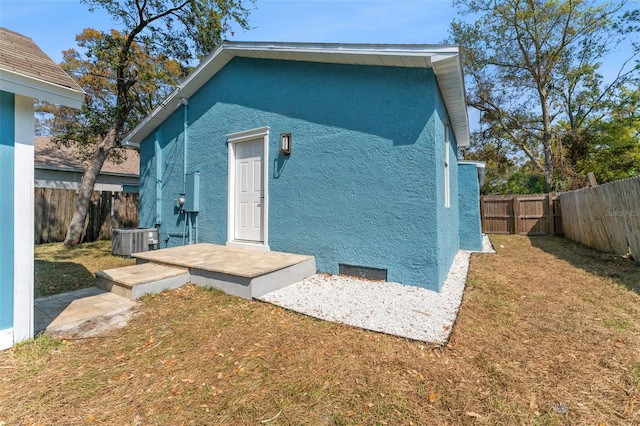 back of house with a fenced backyard, central AC unit, stucco siding, and a yard