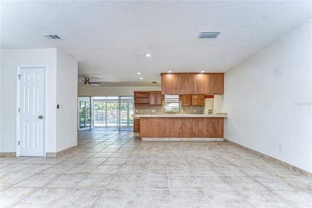 kitchen featuring visible vents, white refrigerator with ice dispenser, a peninsula, and brown cabinetry