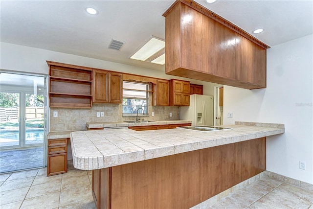 kitchen with a peninsula, a sink, light countertops, tasteful backsplash, and brown cabinets