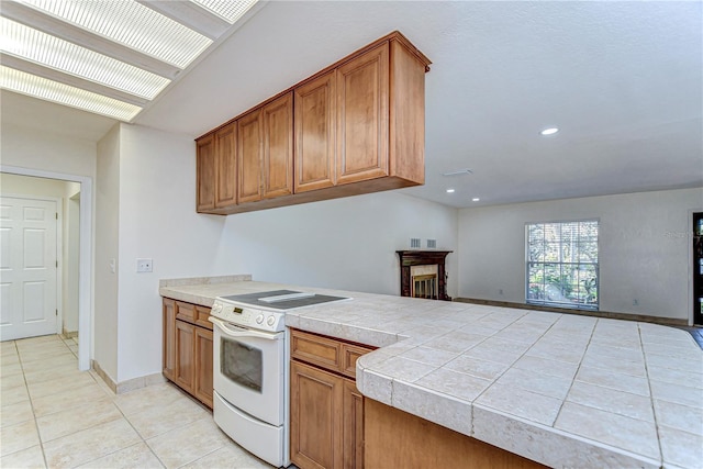 kitchen with a peninsula, electric range, light tile patterned flooring, and brown cabinetry