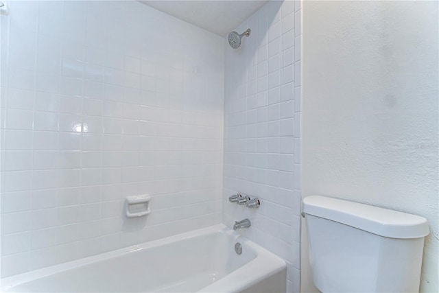 bathroom featuring toilet, a textured wall, and shower / washtub combination