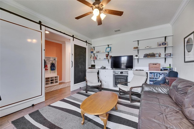 living room featuring visible vents, a barn door, ornamental molding, wood finished floors, and a ceiling fan