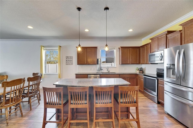 kitchen featuring a kitchen island, crown molding, appliances with stainless steel finishes, a kitchen breakfast bar, and a sink