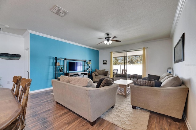 living room with wood finished floors, visible vents, ornamental molding, ceiling fan, and a textured ceiling