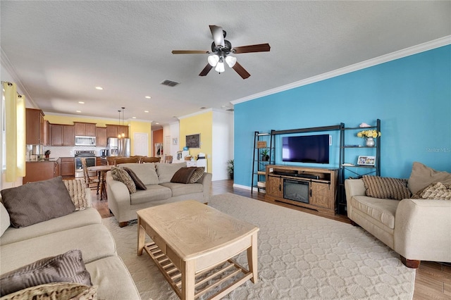 living area with visible vents, ornamental molding, light wood-style flooring, a textured ceiling, and a ceiling fan