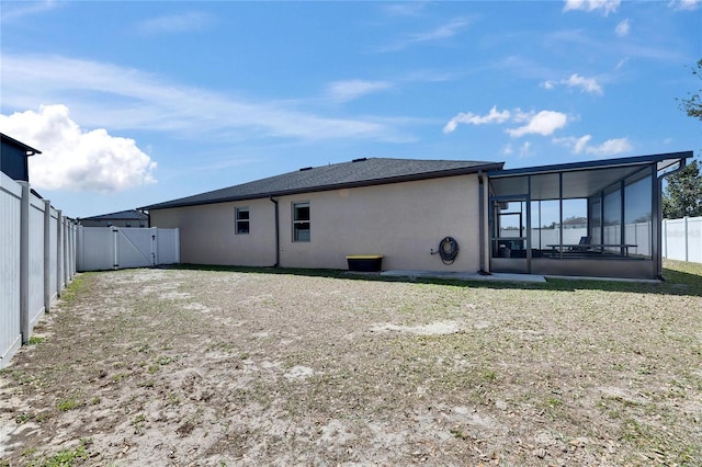 back of house with a gate, stucco siding, a fenced backyard, and a sunroom