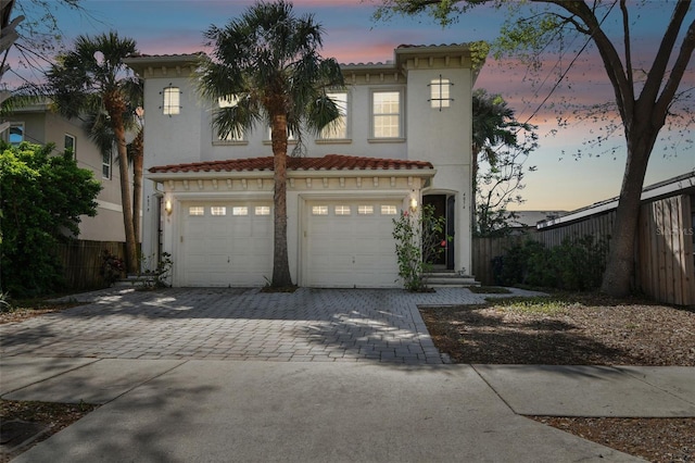 mediterranean / spanish-style home with a tile roof, decorative driveway, fence, and stucco siding