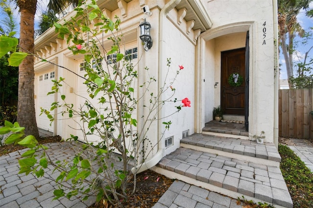 doorway to property featuring stucco siding and fence