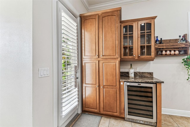 bar featuring light tile patterned floors, beverage cooler, baseboards, ornamental molding, and a bar