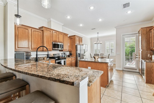 kitchen with light tile patterned floors, a kitchen island, a peninsula, appliances with stainless steel finishes, and brown cabinets