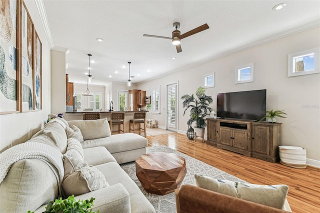 living area featuring a ceiling fan, recessed lighting, crown molding, light wood finished floors, and baseboards