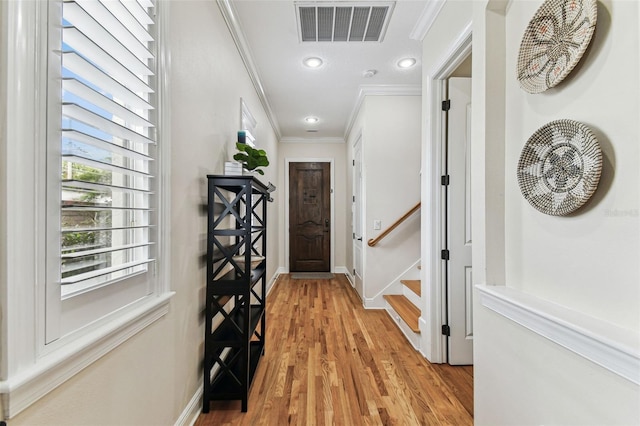 entryway with light wood finished floors, visible vents, baseboards, and ornamental molding