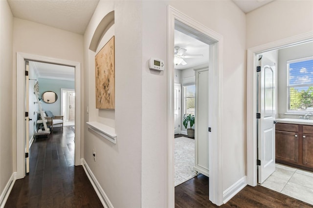 hall with dark wood finished floors, baseboards, and a sink