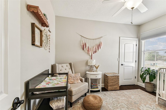 living area with ceiling fan, baseboards, a textured ceiling, and wood finished floors