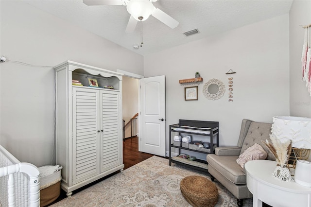 living area with visible vents, ceiling fan, vaulted ceiling, wood finished floors, and a textured ceiling