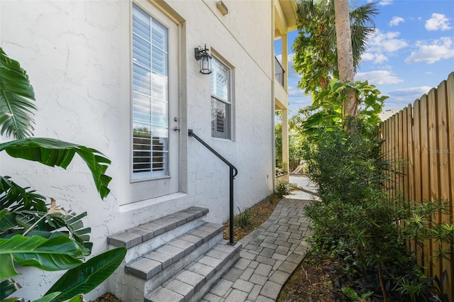 view of exterior entry with stucco siding and fence