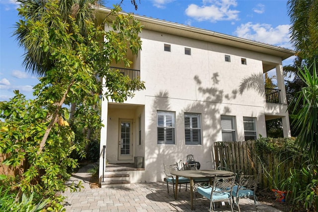 rear view of house with a patio area, stucco siding, a balcony, and fence