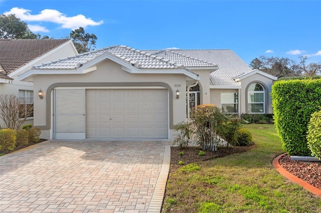 ranch-style house featuring a tiled roof, a front yard, stucco siding, decorative driveway, and a garage