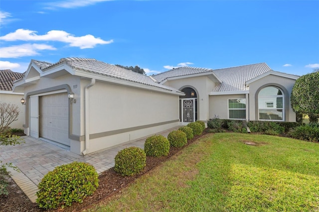 view of front of property with a front lawn, a tiled roof, a garage, and stucco siding