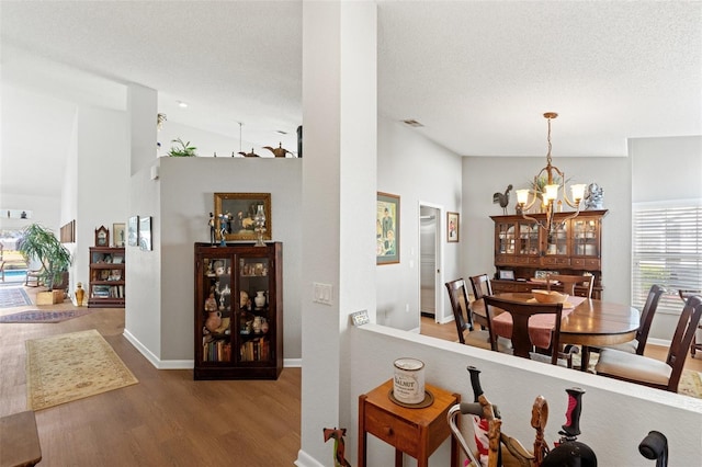 dining room featuring wood finished floors, baseboards, lofted ceiling, a textured ceiling, and a notable chandelier