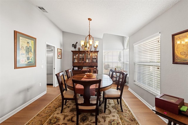 dining area featuring visible vents, a textured ceiling, light wood-type flooring, and an inviting chandelier