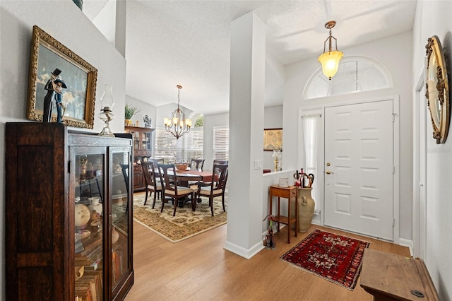 foyer with an inviting chandelier, vaulted ceiling, light wood finished floors, and a textured ceiling