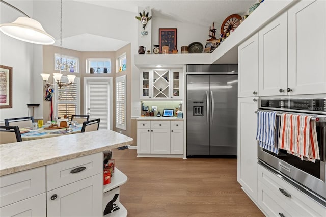 kitchen featuring light wood-style flooring, white cabinetry, appliances with stainless steel finishes, a chandelier, and vaulted ceiling