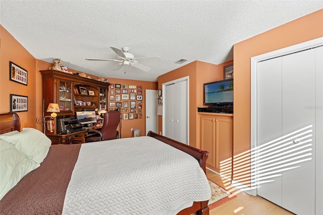 bedroom with a textured ceiling, a ceiling fan, visible vents, and multiple closets