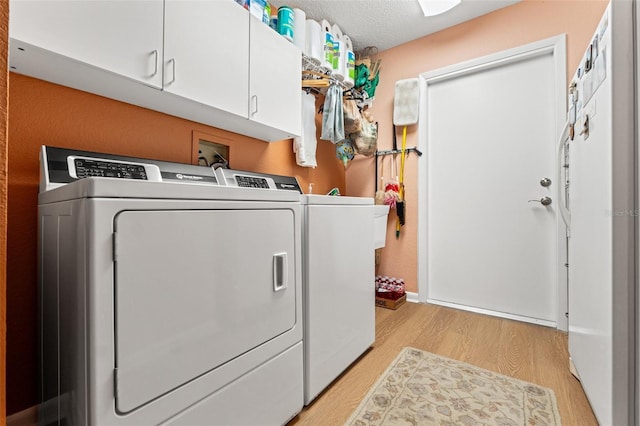 laundry area with cabinet space, light wood-style flooring, washing machine and dryer, and a textured ceiling