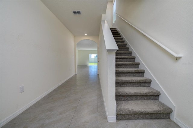 staircase with tile patterned floors, arched walkways, visible vents, and baseboards