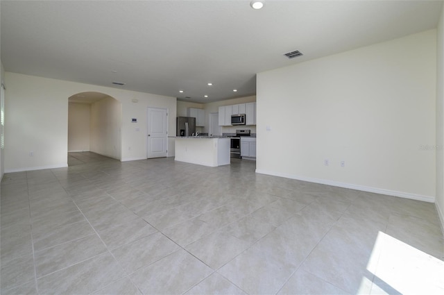 unfurnished living room with light tile patterned floors, visible vents, baseboards, recessed lighting, and arched walkways