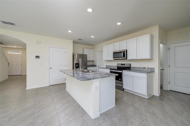 kitchen featuring an island with sink, arched walkways, a sink, appliances with stainless steel finishes, and white cabinetry