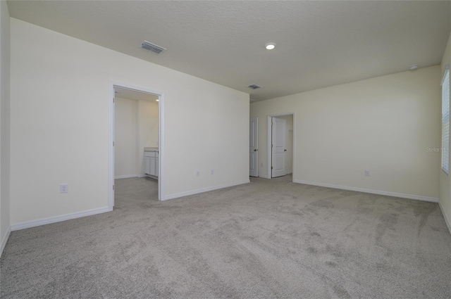 spare room featuring visible vents, light carpet, a textured ceiling, and baseboards