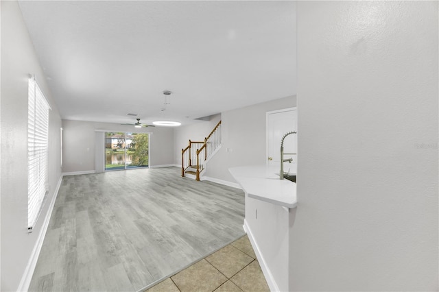 unfurnished living room featuring stairs, light tile patterned floors, a ceiling fan, and baseboards