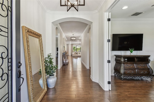 foyer with visible vents, arched walkways, dark wood-style flooring, crown molding, and a chandelier