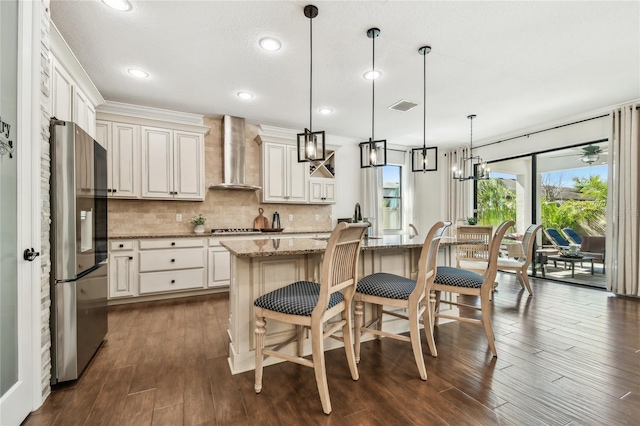 kitchen featuring tasteful backsplash, a center island, wall chimney range hood, light stone countertops, and appliances with stainless steel finishes