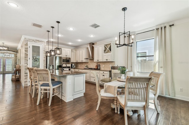 kitchen featuring a sink, visible vents, a notable chandelier, and wall chimney range hood