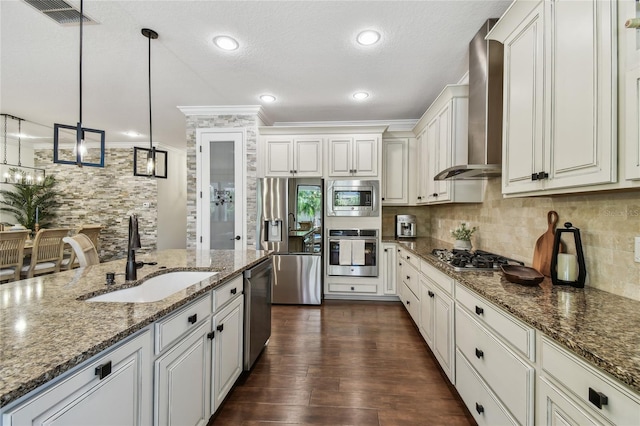 kitchen featuring visible vents, a sink, decorative backsplash, appliances with stainless steel finishes, and wall chimney exhaust hood