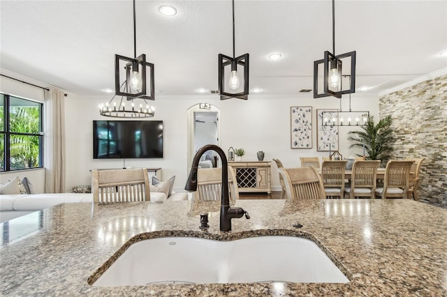 kitchen featuring crown molding, open floor plan, stone counters, and a sink