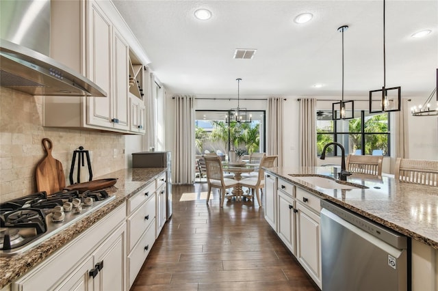 kitchen featuring a sink, stainless steel appliances, a chandelier, and wall chimney range hood