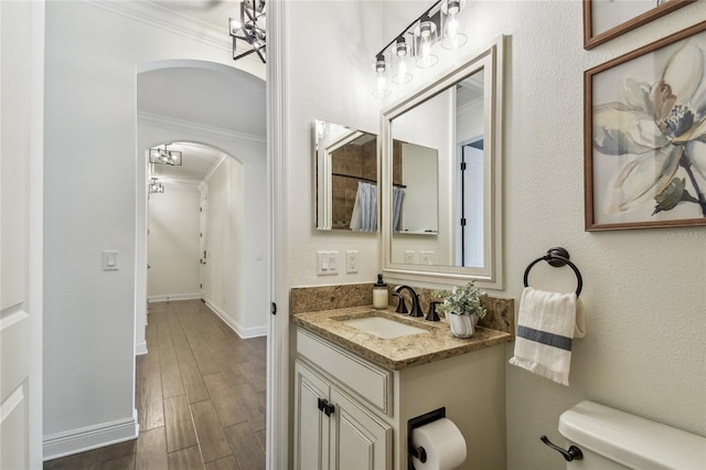 bathroom featuring wood finish floors, toilet, ornamental molding, baseboards, and vanity