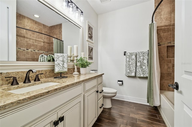 bathroom featuring vanity, baseboards, wood finish floors, tiled shower / bath combo, and toilet