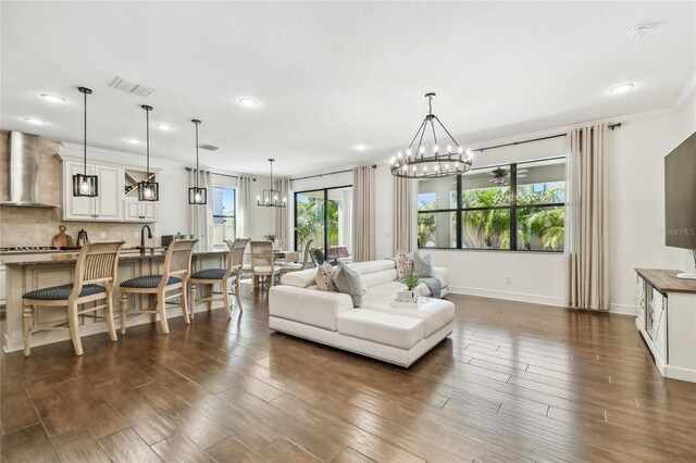 8307 Bluevine Sky Dr, Land O Lakes, FL 34637 - living room with a chandelier, dark wood-type flooring, recessed lighting, baseboards, and crown molding