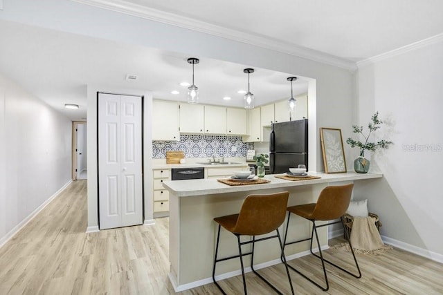 kitchen with a peninsula, light wood-style flooring, ornamental molding, black appliances, and light countertops