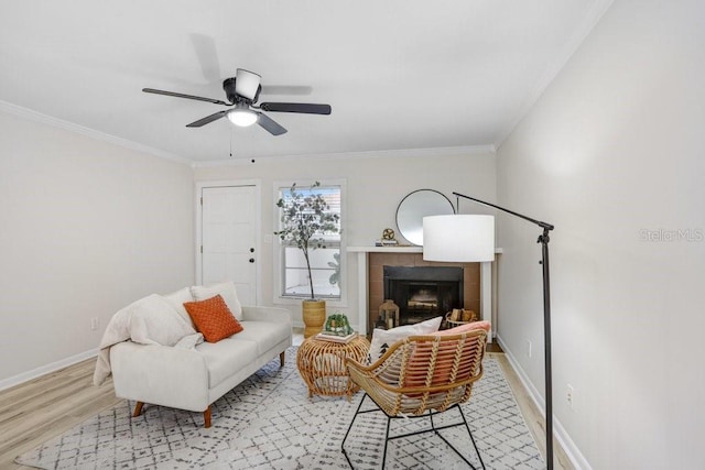 living room with light wood finished floors, a tiled fireplace, crown molding, and baseboards