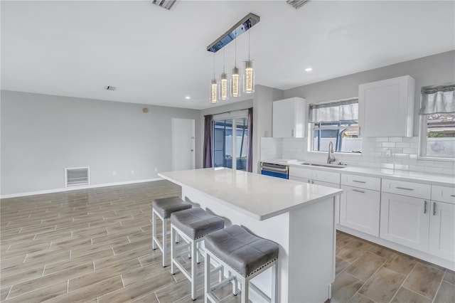 kitchen featuring wood finish floors, visible vents, a sink, tasteful backsplash, and a center island