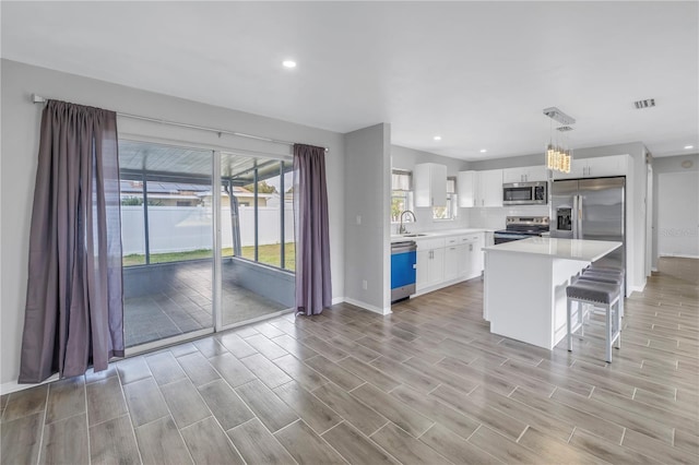 kitchen with a sink, stainless steel appliances, white cabinets, light countertops, and wood tiled floor