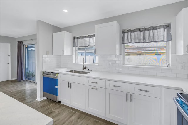 kitchen featuring wood tiled floor, dishwasher, light countertops, white cabinets, and a sink