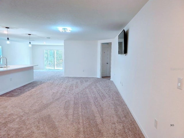 unfurnished living room with a textured ceiling, light colored carpet, baseboards, and a sink